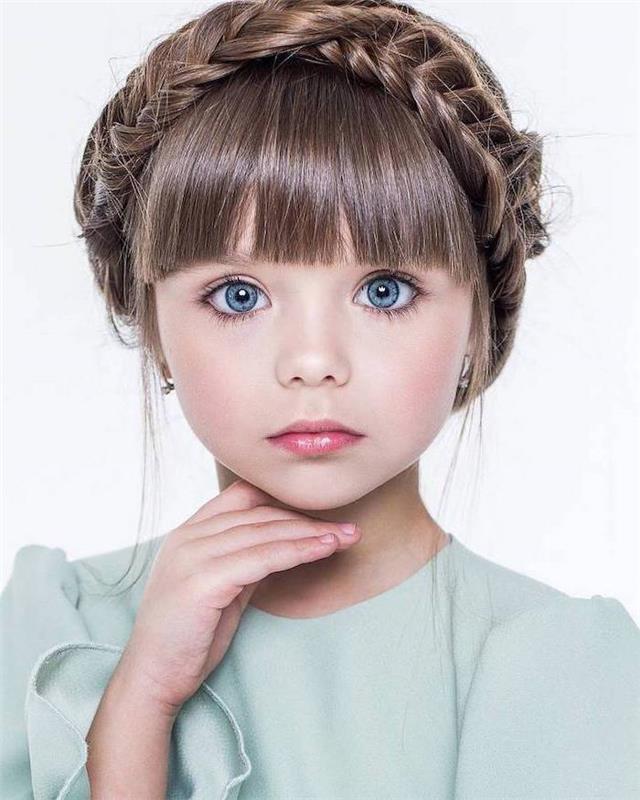 Karūninė pynė ant ilgų plaukų su kirpčiukais, mėlynos akys, maža mergaitė ir žavinga mėlyna suknelė, vaikiška šukuosena, pintinė šukuosena, kaip formuoti plaukus