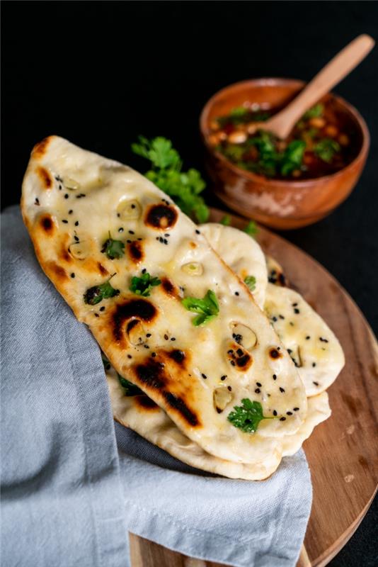 tahta kesme tahtasına yerleştirilmiş sarımsaklı maydanozlu naan ekmeği, naan ekmeği tarifi, yanında mavi koton