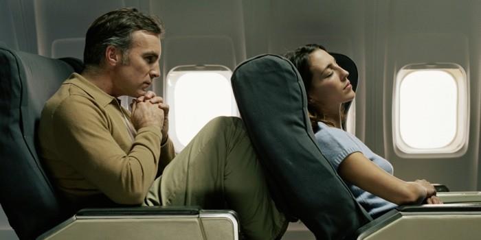 Keleivis vyriškis, keliais atsirėmęs į keleivio sėdynę lėktuve