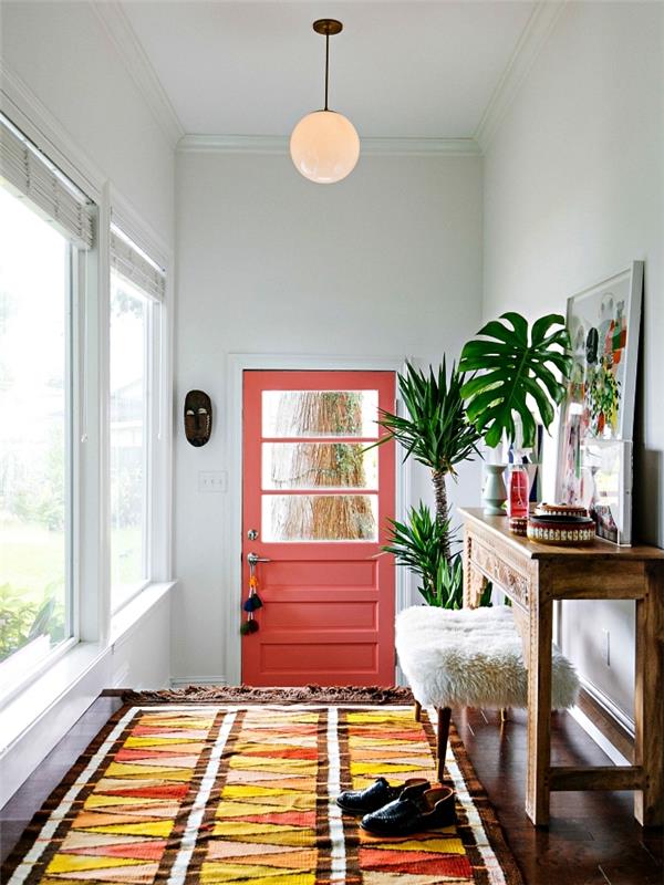 boemsko elegantna dekoracija hodnika z raznobarvno grafično preprogo, vhodnimi vrati v barvi koral in starodobno leseno konzolo