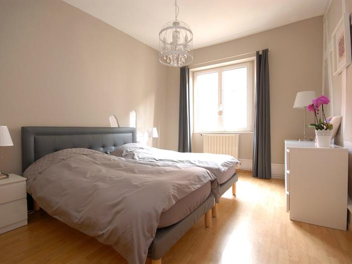 Preprosta spalnica za odrasle z veliko sivo posteljo, nočno omarico iz bele ikee, jasna dekoracija glavne spalnice
