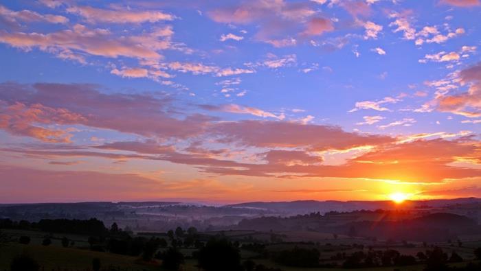 purpurinio dangaus peizažas, oranžinė saulė virš lygumos, mažas Toskanos kaimelis, alyvmedžių giraitės, rami vakaro atmosfera