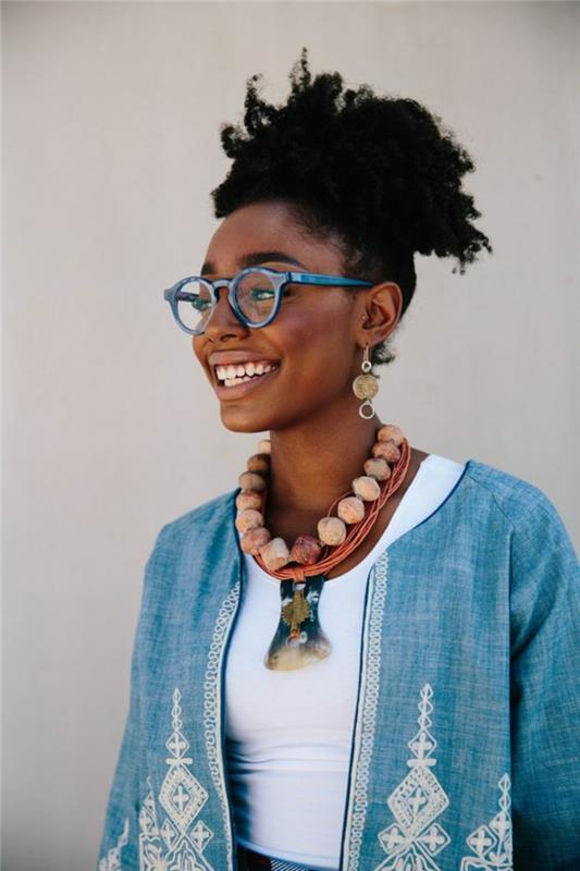 mėlyna moteriška striukė su arabiškais papuošimais ir etniniais baltais raštais, afrikietišku motyvu, afrikietiška mada, kaklo papuošalas rožinės spalvos su dideliais kamuoliukais, dideli hipsteriniai akinių rėmeliai mėlynos spalvos